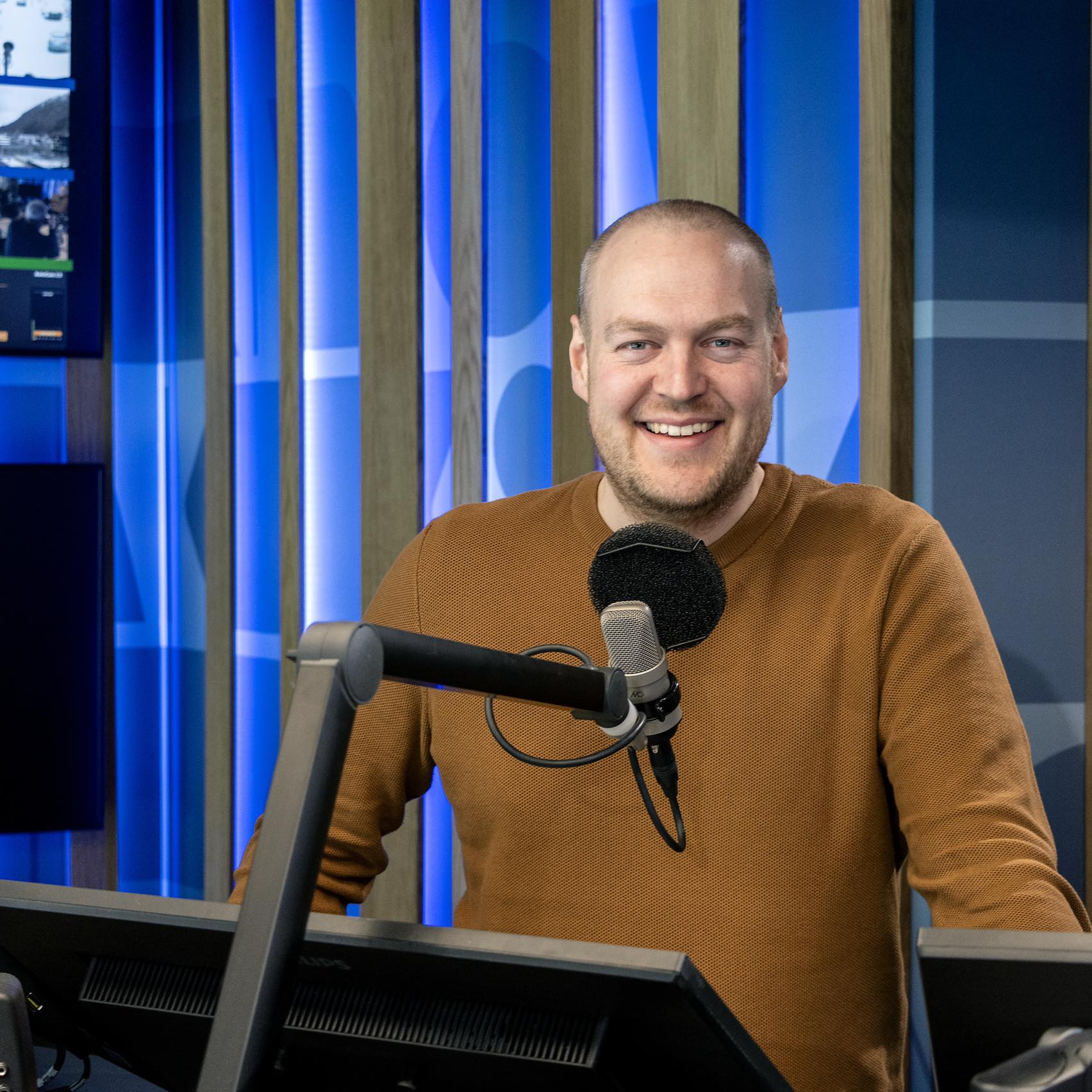 Bilde av Fredrik Johan Helland i eit radiostudio. Han står bak ein mikrofon og smiler.