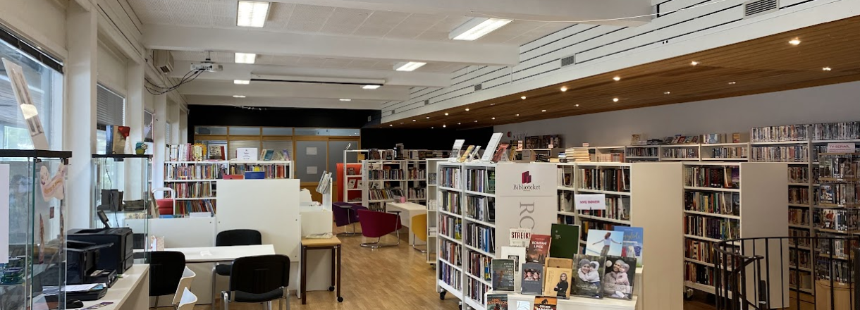 Bilde frå biblioteket som visar utstilling av nye bøker, publikums-PC, og innover boksamlinga mot kafeen til hotellet.